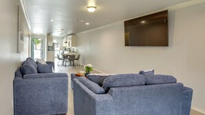 Un salon moderne avec deux canapés gris, un téléviseur à écran plat fixé au mur et un coin repas à l’arrière-plan.