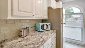 Une cuisine avec des meubles blancs, un grille-pain turquoise et une fenêtre avec des stores.