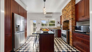 Una cocina con armarios de madera, una isla central con fruta, un horno de ladrillo y piso a cuadros.