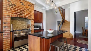 Una cocina con pared de ladrillo, electrodomésticos de acero inoxidable, una isla de madera y piso a cuadros.