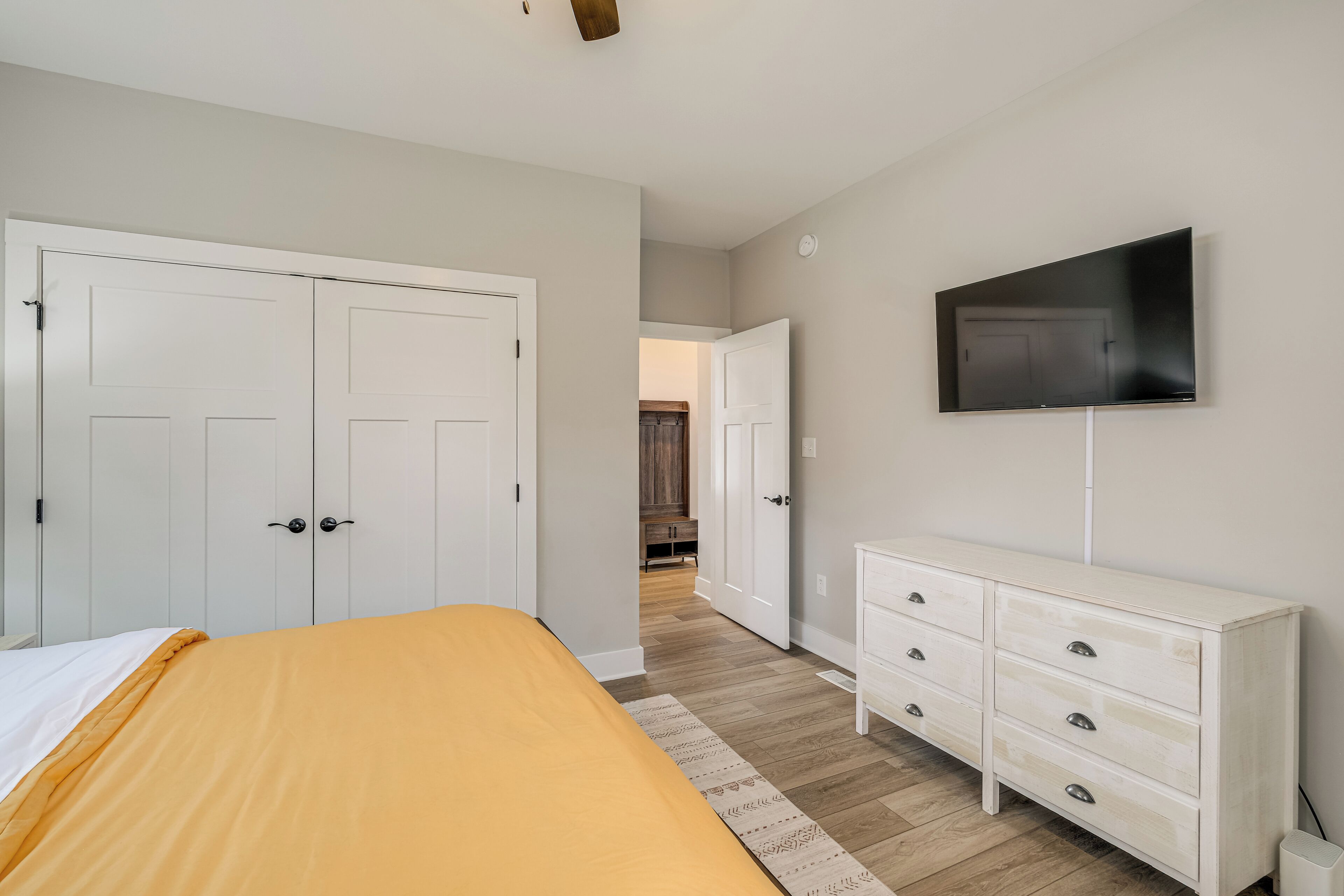 A bedroom with a bed, a dresser, a television, and a hallway leading to another room.