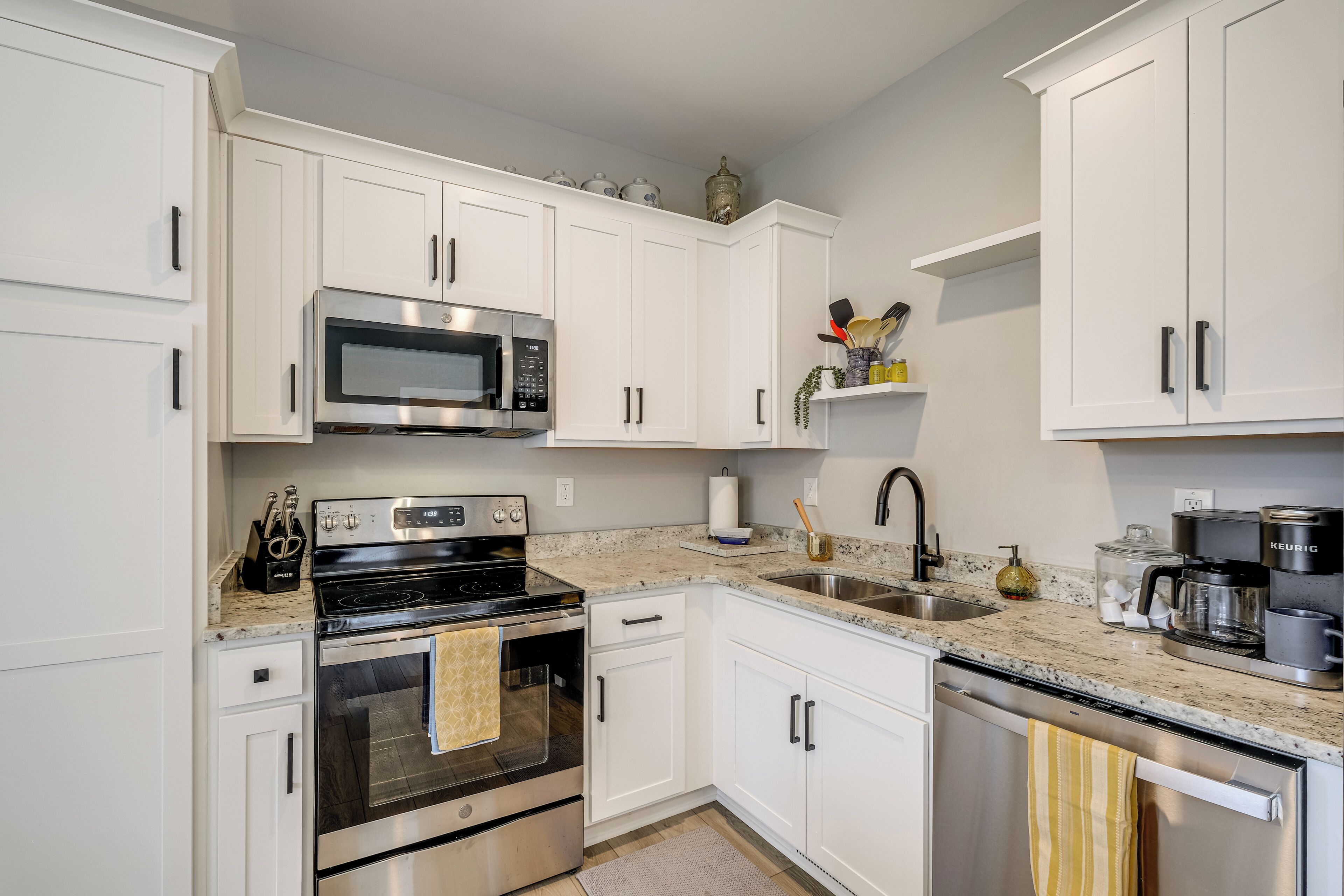 A modern kitchen with white cabinets, stainless steel appliances, a granite countertop, and a dishwasher.