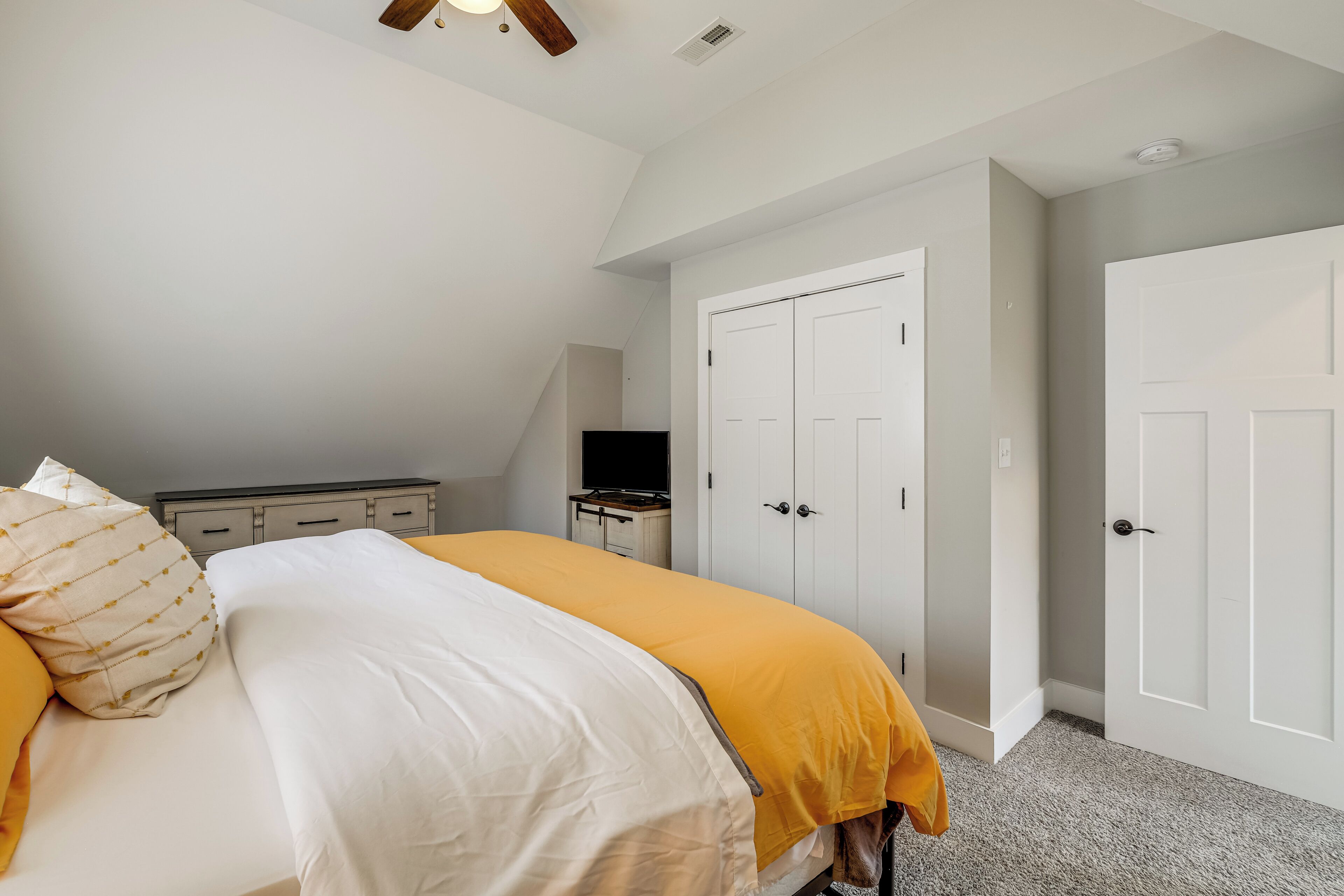 A bedroom with a bed, a dresser, a TV, and two doors.