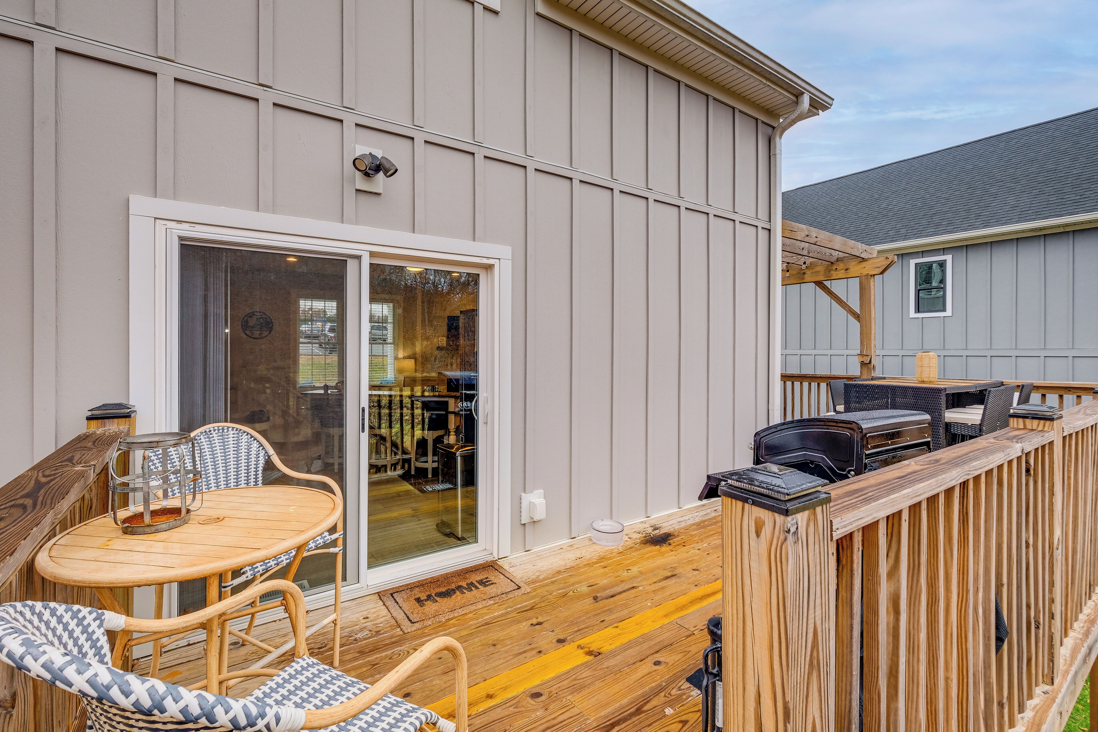 Una terraza con mobiliario exterior, una parrilla y una puerta corrediza de vidrio que da a un espacio interior.