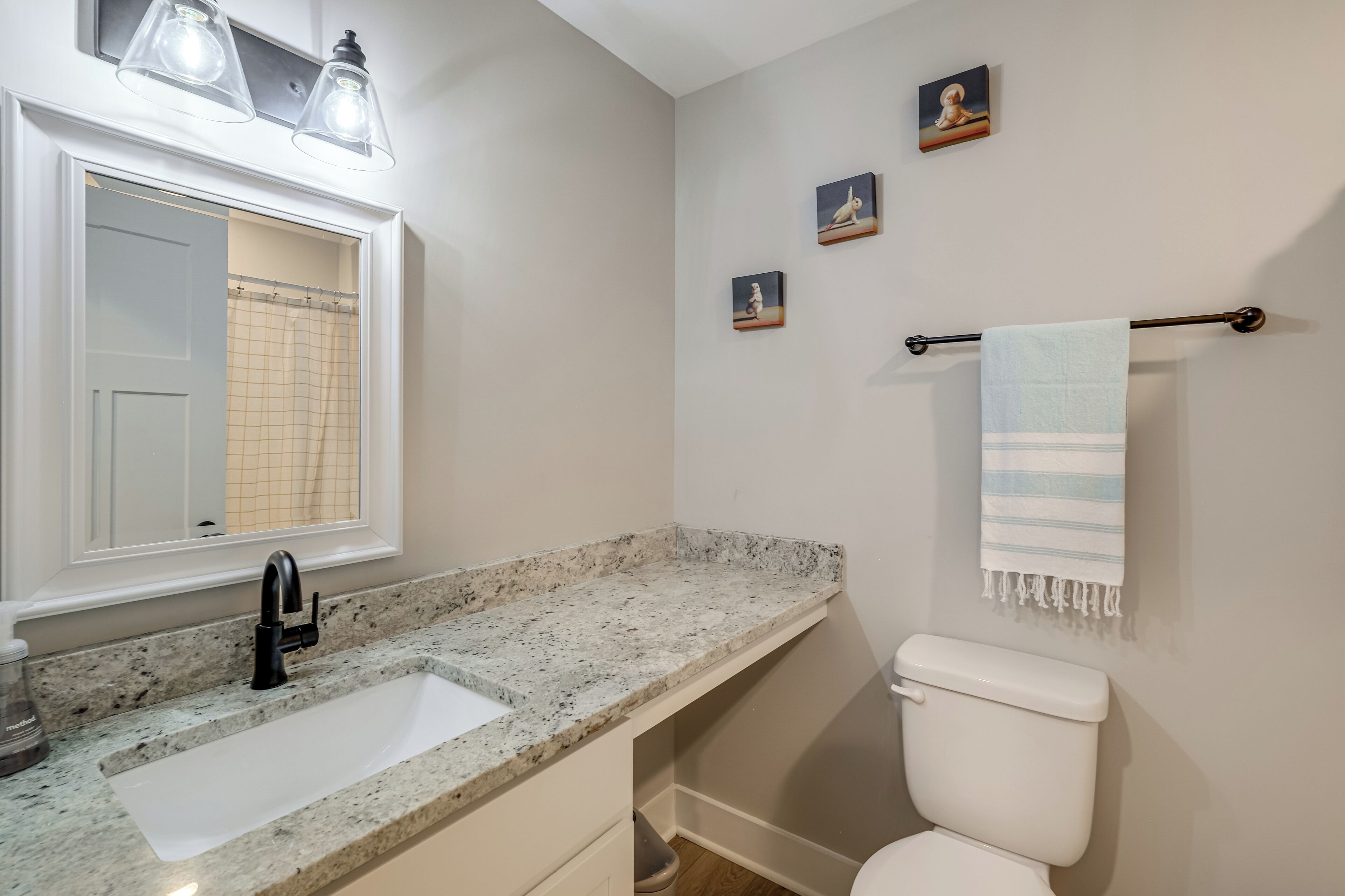 A bathroom with a white sink, black faucet, and a towel rack with a towel. There are three framed pictures on the wall.