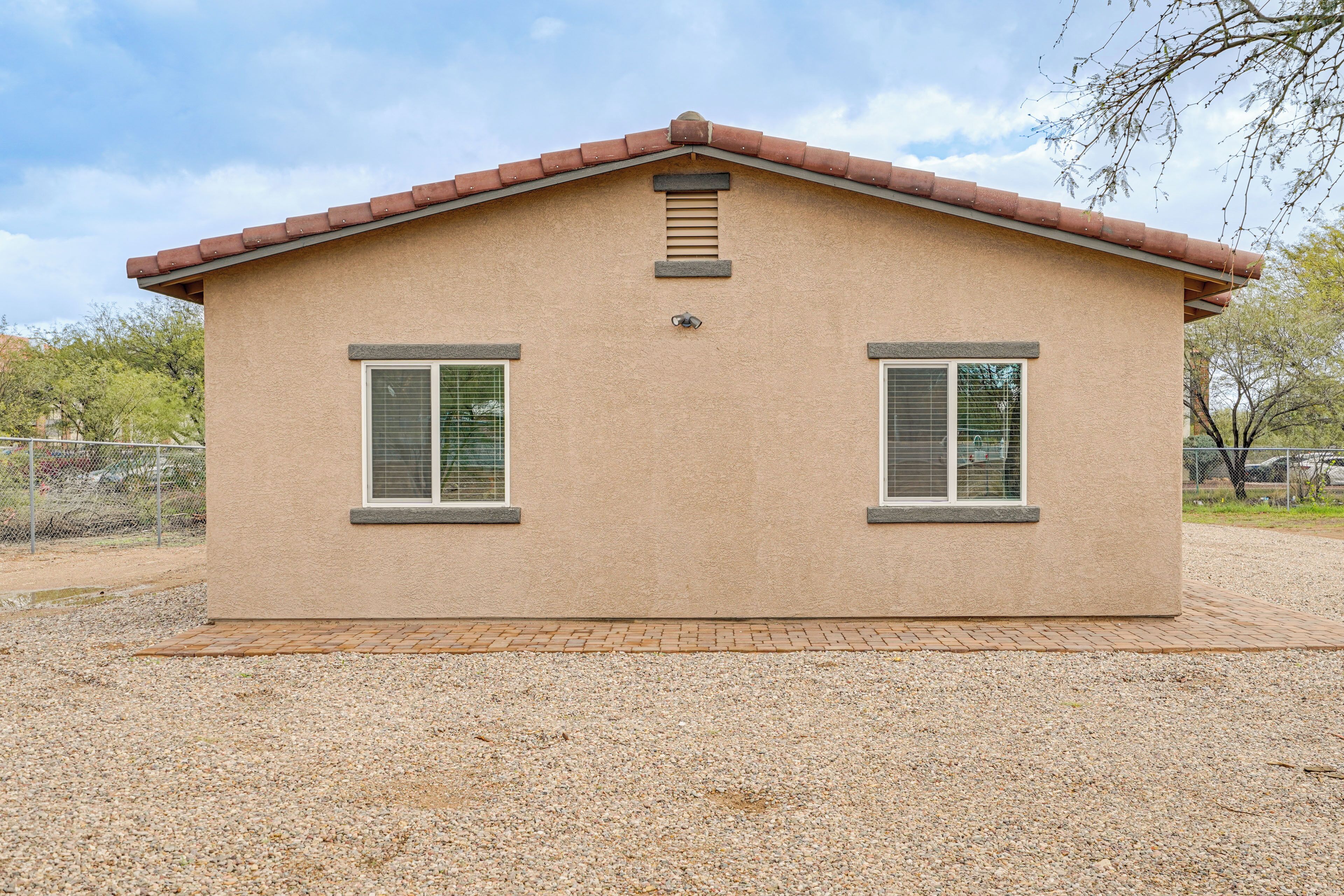 A single-story building with a brown stucco exterior, two windows with shutters, and a small vent on the roof.