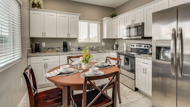 A modern kitchen with white cabinets, a stainless steel refrigerator, a microwave, and a stove. There is a dining table with chairs and a vase of flowers. - Near Casino & Dtwn! Tucson Townhome: Saguaro NP (Tucson)