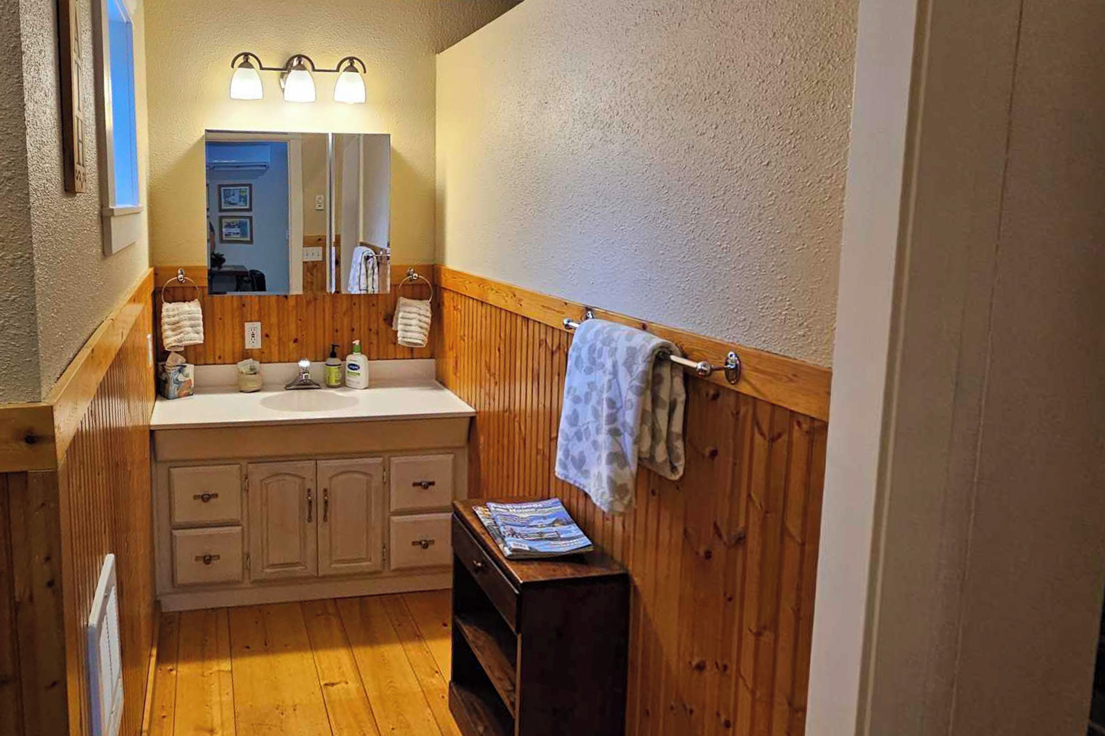 Un baño pequeño con tocador de madera, un espejo con tres luces y un perchero para toallas.