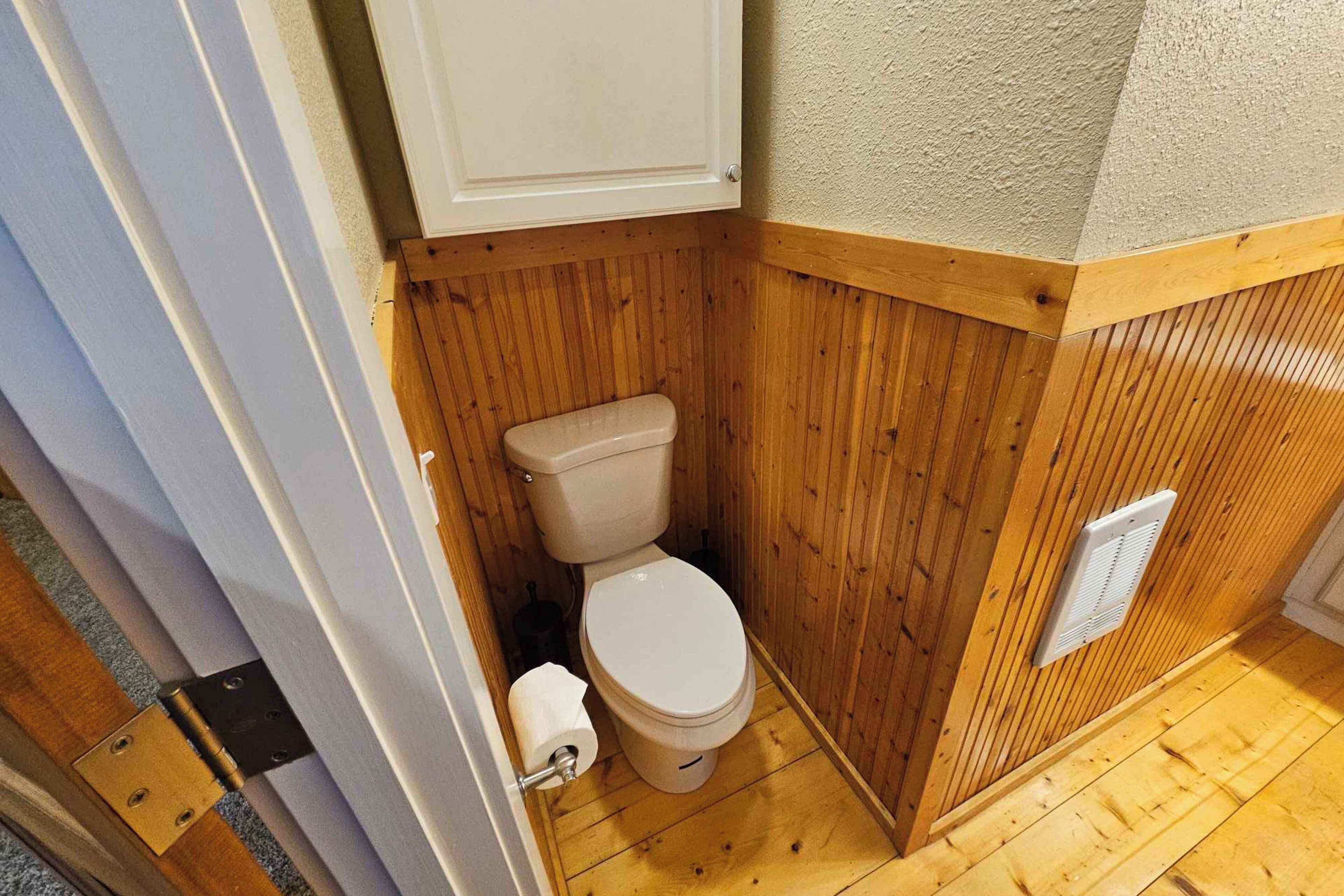 A small, compact bathroom with wooden paneling, a white toilet, and a visible vent on the wall.
