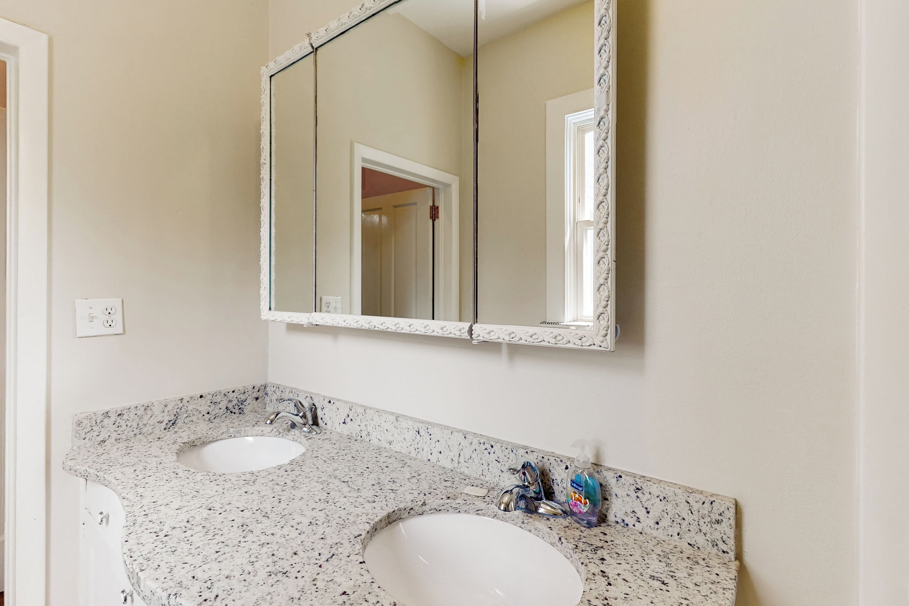 A bathroom with two sinks, a large mirror, and a door leading to another room.