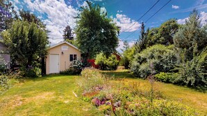 A small, single-story house with a garage, surrounded by a well-maintained garden with various plants and flowers. - 2BR Home w/ Mountain View, W & D, Private Yard (Ashton)