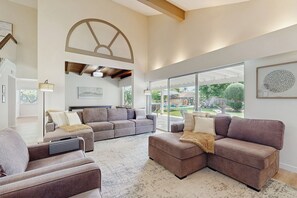 A spacious living room with a sectional sofa, a coffee table, and a large window offering a view of the outdoors. - 4BR Dog-friendly Home w/ Pool, Spa, Grill & A/C (Mission Viejo)