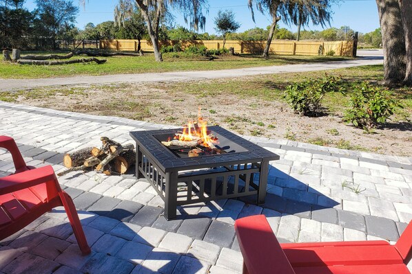 A fire pit table with logs, surrounded by red chairs, on a paved patio. - Countryside 3BR on 1 Protected Acre w/ Grill (Sanford)