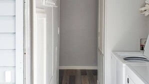 Ein Waschraum mit einer Waschmaschine, einem Wäscheständer und einer Tür zu einem Flur mit Holzboden.