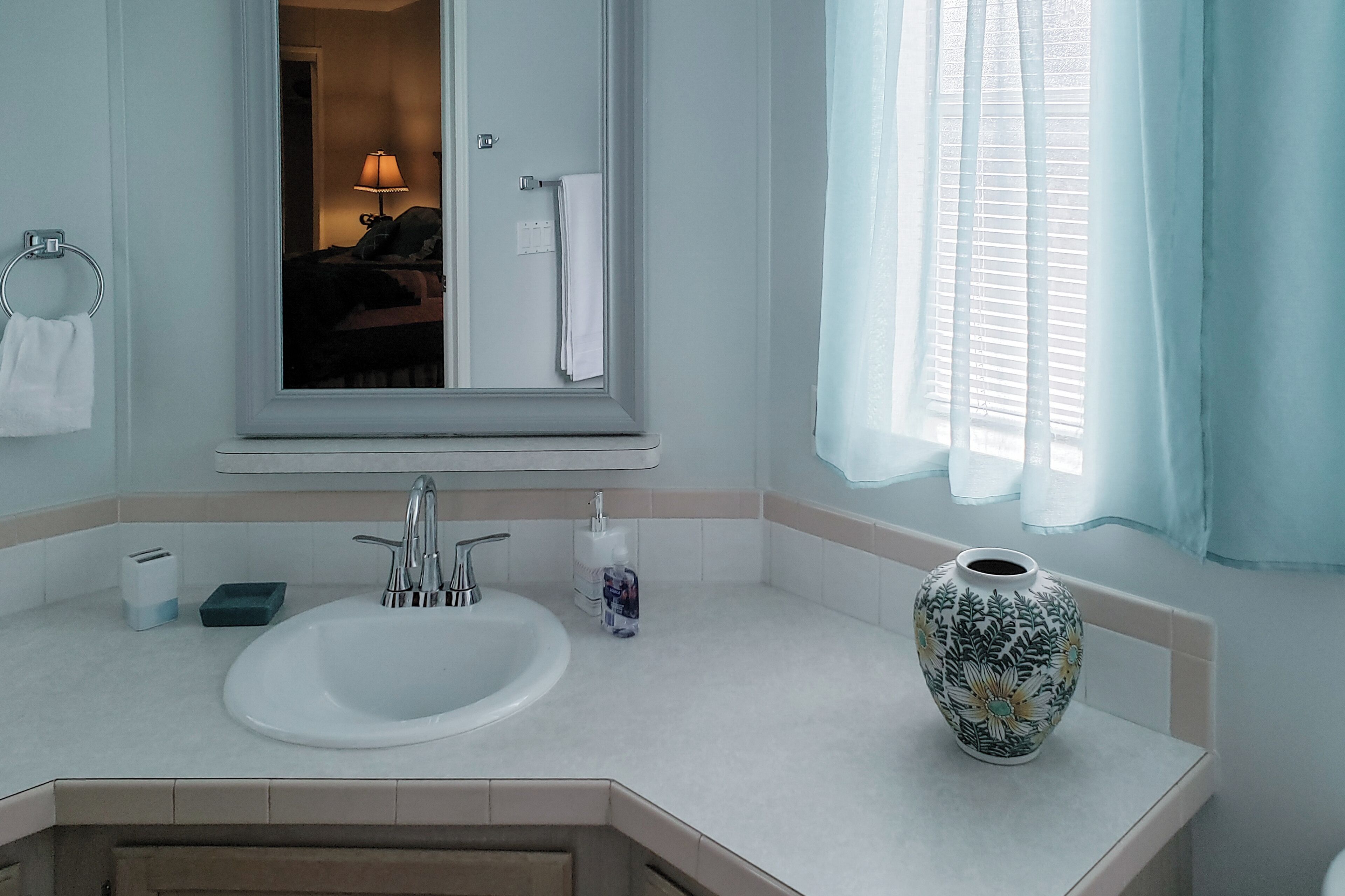 A bathroom with a sink, mirror, and a vase on the counter.