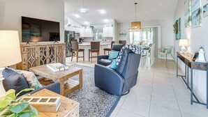 A spacious living room with a sofa, coffee table, and TV. There is a kitchen in the background with modern appliances and a dining area. - Golf, Shop & Unwind: Home w/ Patio in The Villages (The Villages)