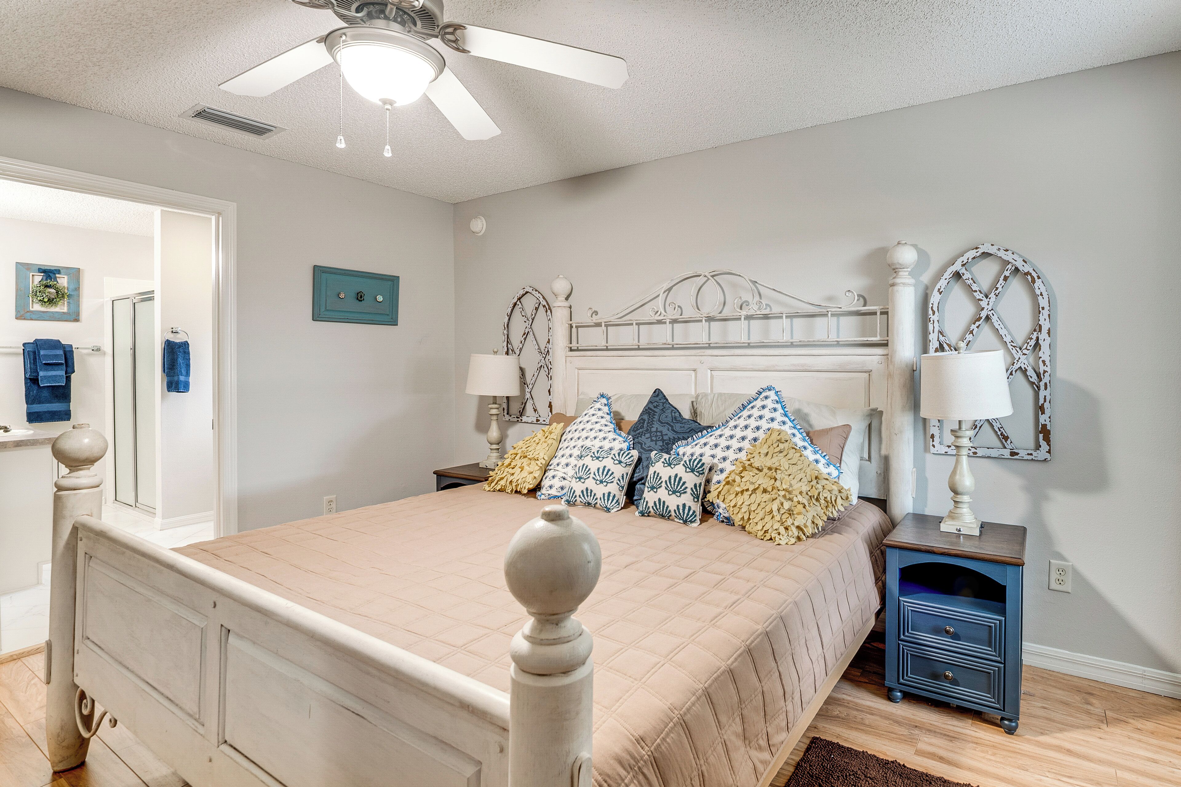 A bedroom with a bed, bedside tables, a ceiling fan, and a door leading to another room.