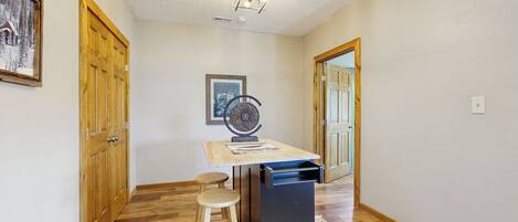 A hallway with wooden flooring, a small table with stools, a ceiling fan, and wooden doors.