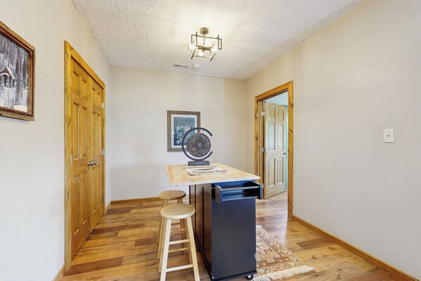 A hallway with wooden flooring, a small table with stools, a ceiling fan, and wooden doors.