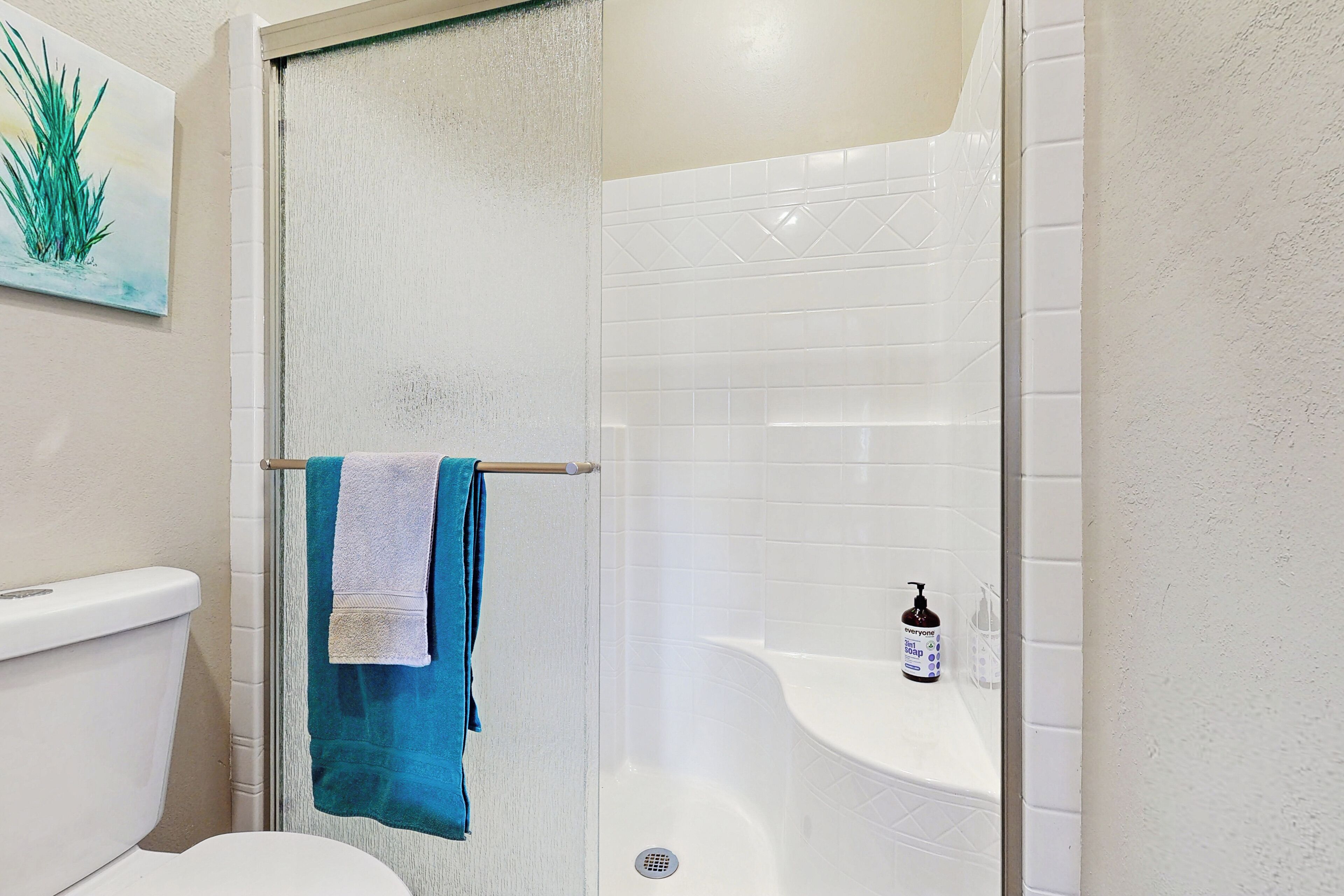 A bathroom with a shower, toilet, and a sink with a soap dispenser.
