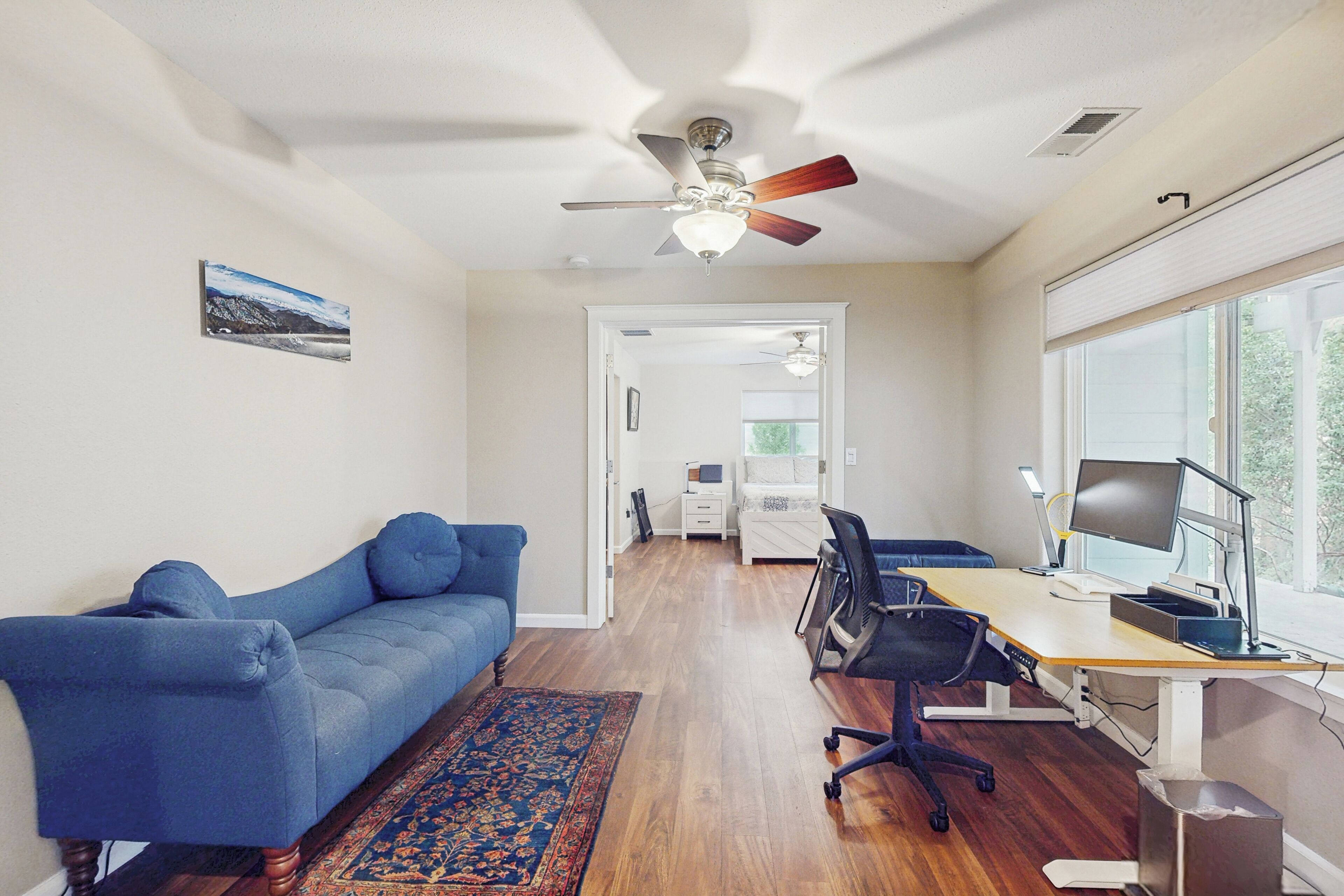 A room with a blue sofa, a wooden desk with a computer, and a ceiling fan.