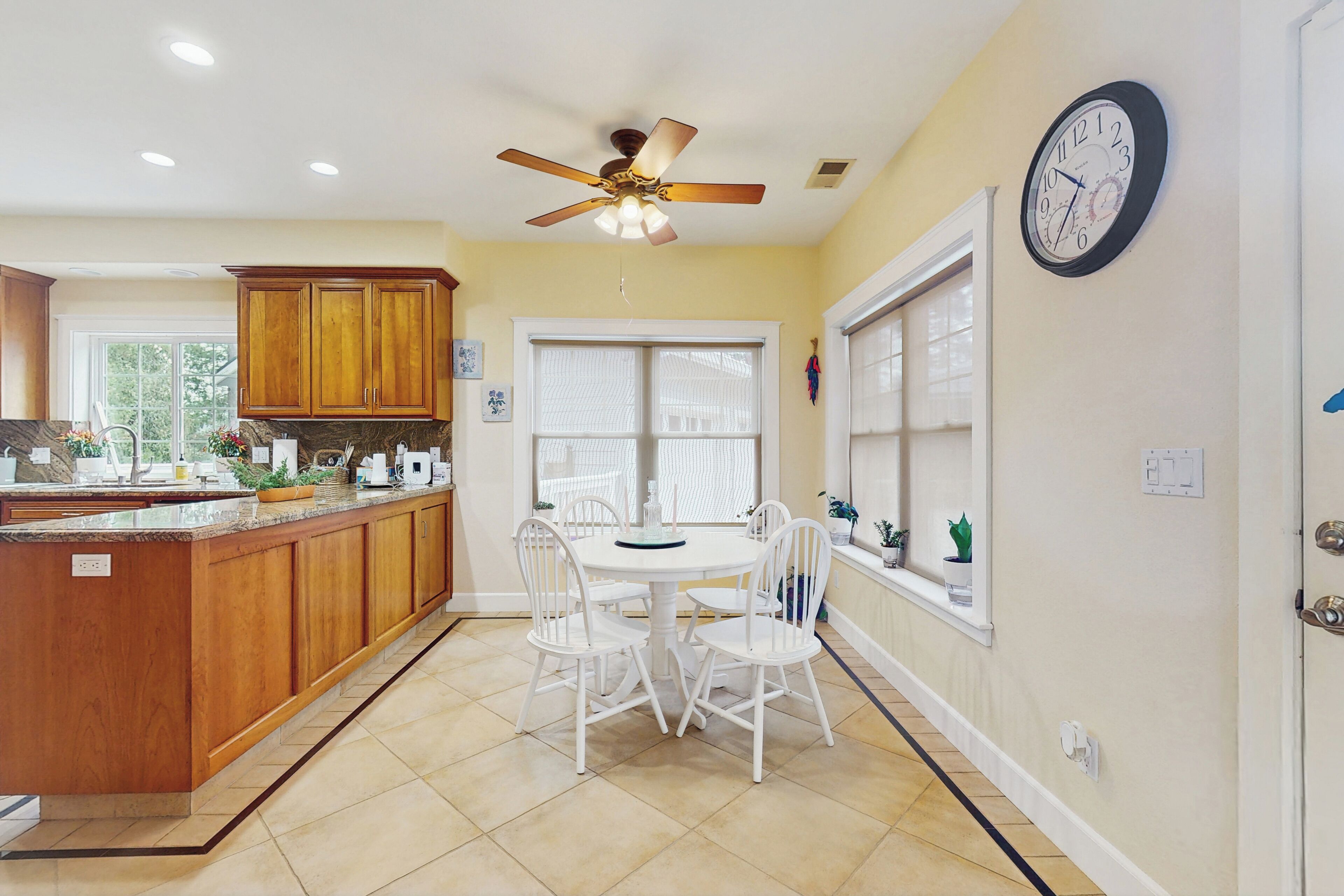 A kitchen with a central island, white chairs, a ceiling fan, and a clock on the wall.