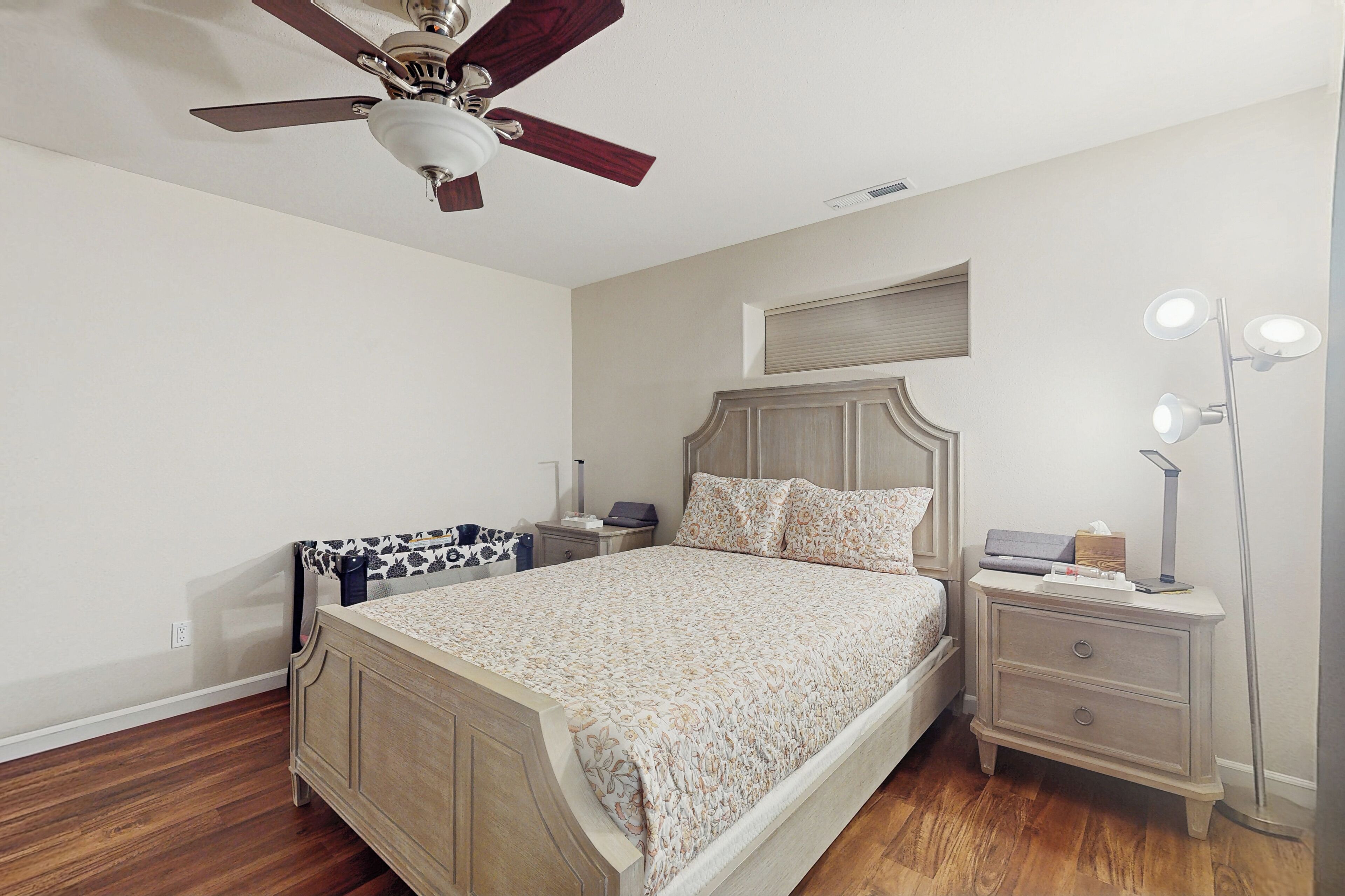 A bedroom with a wooden bed, a nightstand with a lamp, a ceiling fan, and a bedside table with a lamp.