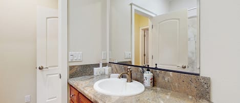 A bathroom with a white sink, granite countertop, wooden cabinets, a large mirror, and a ceiling light fixture.
