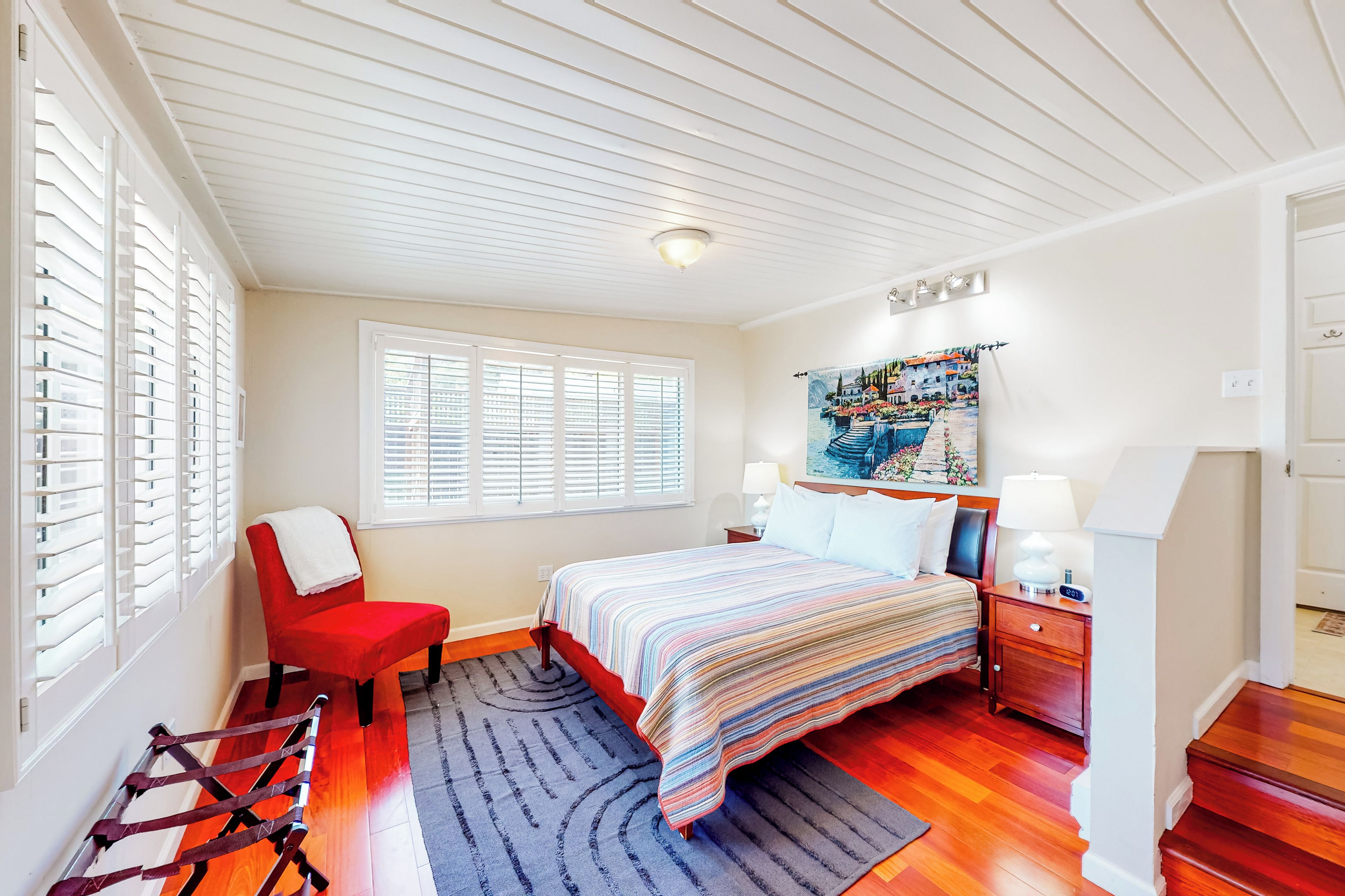 A bedroom with a bed, a chair, a nightstand, a lamp, and a window with blinds.