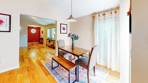 A dining area with a wooden table, bench, and chairs, a hanging light fixture, and a view through a window with sheer curtains. - Centrally Located! Dog-friendly San Rafael Home (San Rafael)