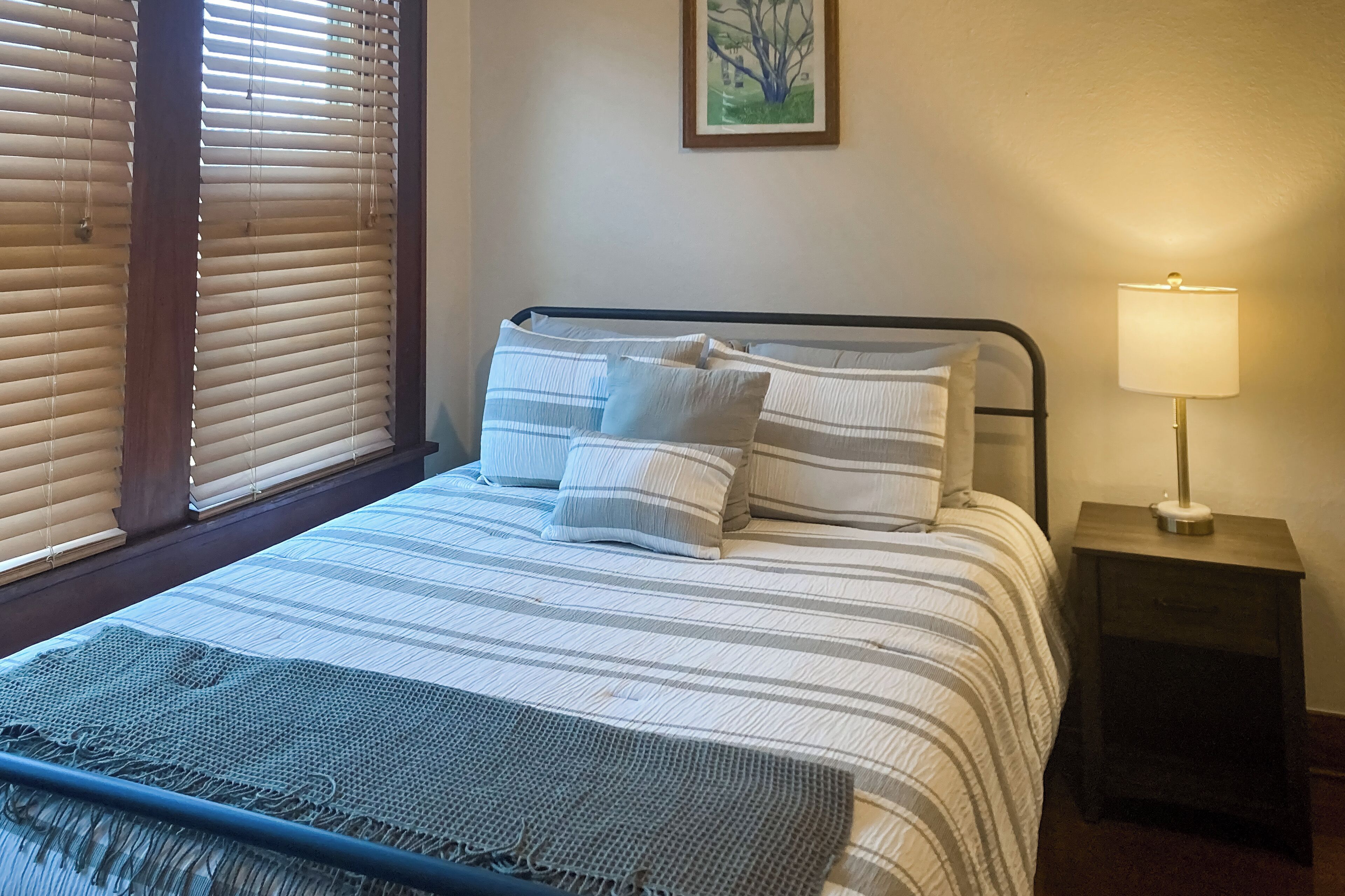 A neatly made bed with striped bedding and pillows, a bedside lamp, and a framed picture on the wall.