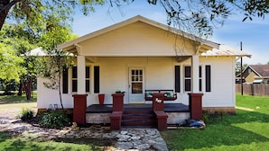A single-story house with a front porch, a stone pathway leading to the door, and a number '207' on the front. - Walkable 1900s Home w/ Porch in Downtown Buda (Buda)