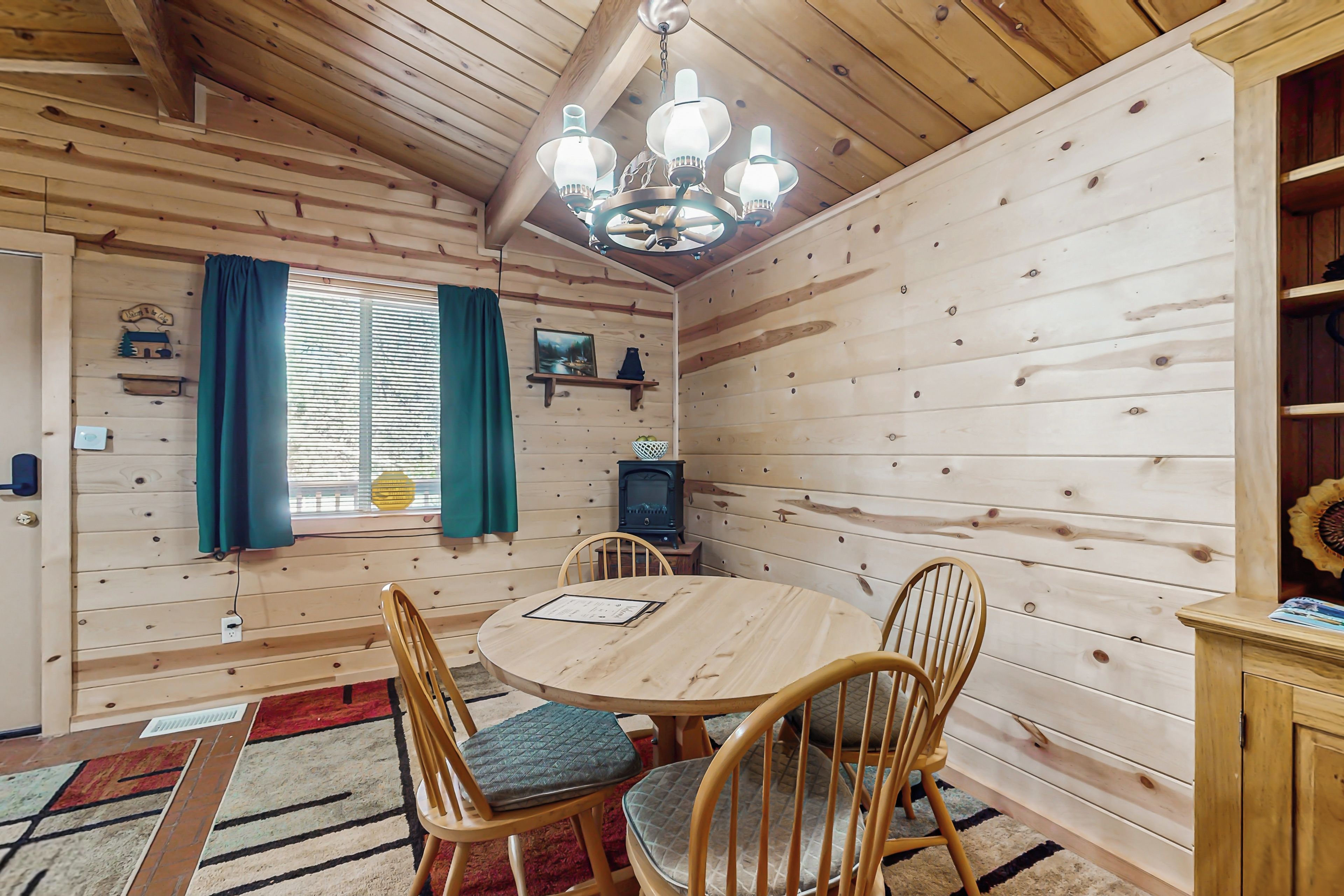 Een houten chaletinterieur met een ronde houten tafel, vier houten stoelen, een kroonluchter, een televisietoestel en een boekenplank.