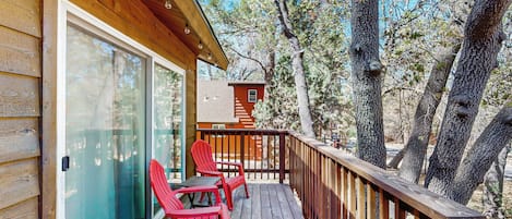 A wooden deck with red chairs and a glass door.