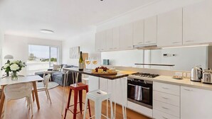 Una cocina moderna con armarios blancos, un comedor con mesa y sillas, y vistas de la ciudad a través de amplias ventanas.