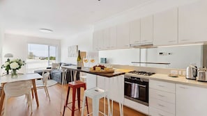 Eine moderne Küche mit weißen Schränken, eine Essecke mit Tisch und Stühlen sowie ein Blick auf die Stadt durch große Fenster.