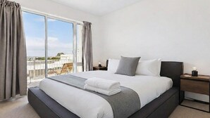 Una habitación de hotel moderna con una cama grande, una mesita de noche y vistas a la ciudad a través de amplios ventanales.