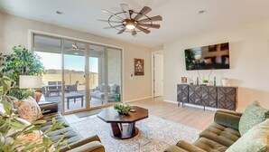 A spacious living room with a large sliding glass door leading to an outdoor patio, a ceiling fan, a flat-screen TV mounted on the wall, and a dark wood cabinet. - Stargazing Haven in Gold Canyon w/ Mtn Views (Gold Canyon)