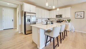 A modern kitchen with white cabinetry, stainless steel appliances, and a central island with bar stools. - Stargazing Haven in Gold Canyon w/ Mtn Views (Gold Canyon)