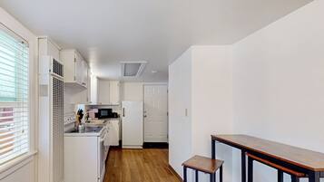 A compact kitchen with white cabinets, a microwave, and a stove. There is a wooden floor and a small wooden table with two stools.