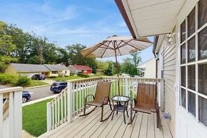 Een houten terras met een tafel, stoelen en een grote parasol, omringd door een witte schutting.