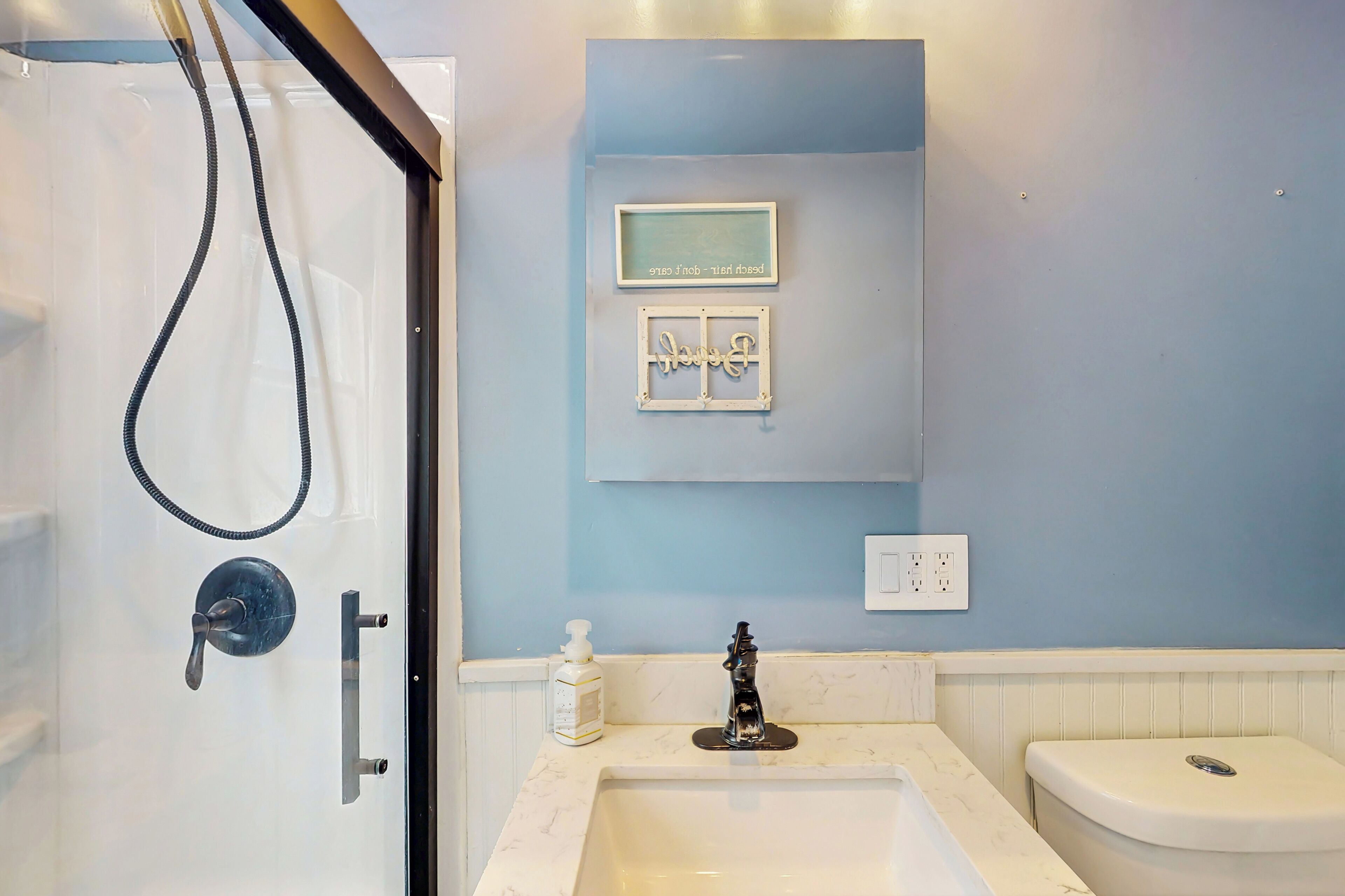 Une salle de bain avec une douche, un lavabo et des toilettes. Il y a deux interrupteurs fixés au mur et un distributeur de savon sur le comptoir.