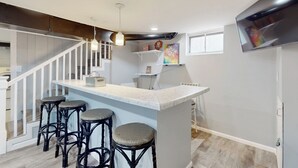 Une cuisine moderne avec un coin bar, des tabourets de bar blancs et un grand téléviseur fixé au mur.
