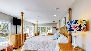 A bedroom with a large bed, a television, a wooden nightstand, and a window with a view of greenery. - Escape the Heat! Lakefront Paradise in Mount Dora (Mount Dora)