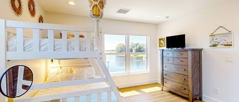 A room with a bunk bed, a vanity with a mirror, a dresser, and a large window with a view of a body of water.