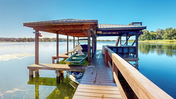 A wooden dock extending into calm water with a covered seating area and a small boat. - Escape the Heat! Lakefront Paradise in Mount Dora (Mount Dora)