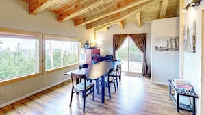 Un comedor amplio con una mesa y sillas de madera, ventanas grandes y vistas a zonas verdes al exterior.