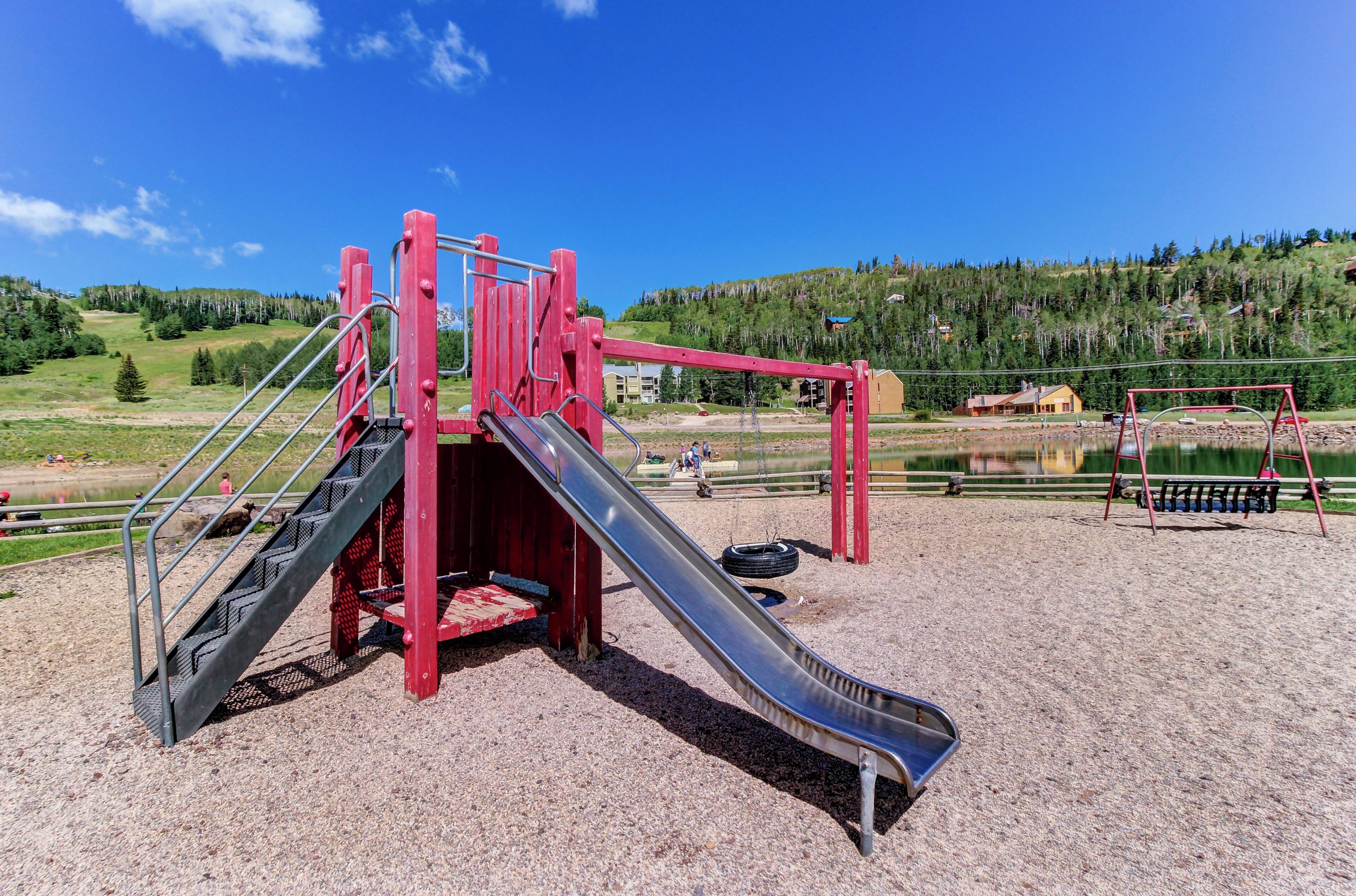 Un parque infantil con un tobogán y una estructura de escalada, rodeado de grava y una vista panorámica de colinas y árboles.