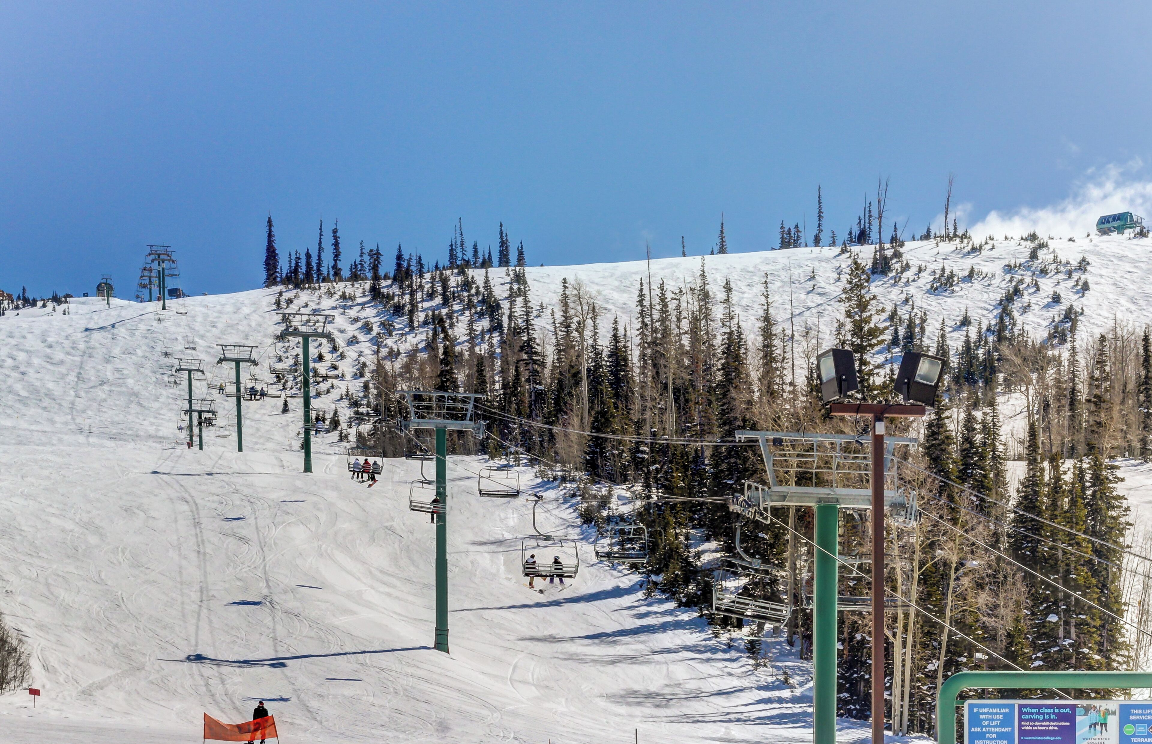 A ski lift system with chairs and cables on a snowy mountain slope.