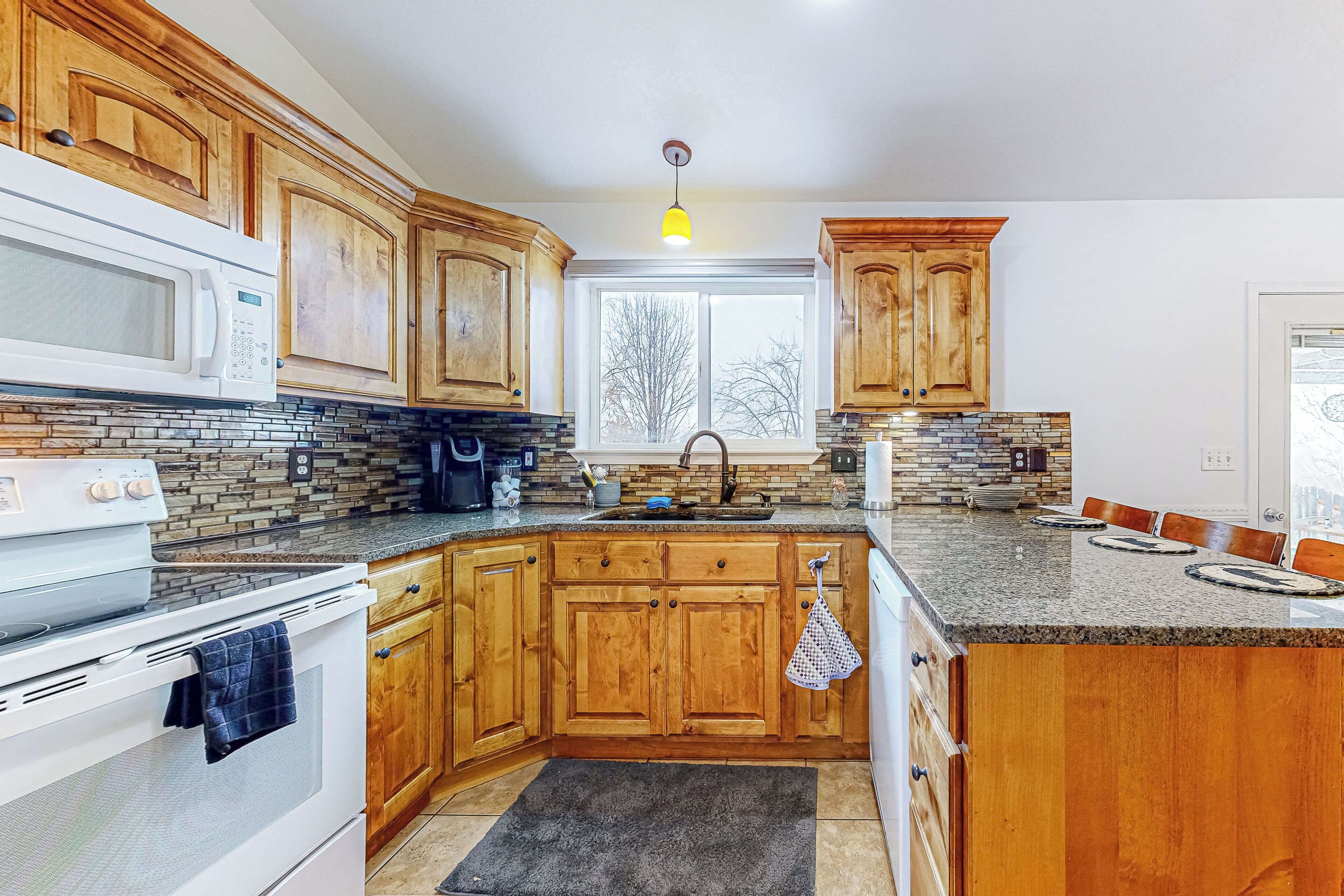 A kitchen with wooden cabinets, a granite countertop, a built-in oven, a microwave, and a window providing natural light.